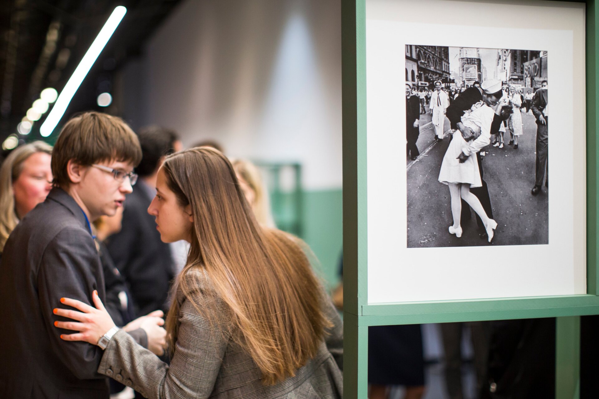 Die Leute sprechen neben einem berühmten Foto von Alfred Eisenstaedt, das zeigt, wie ein Matrose am VJ-Day eine Krankenschwester auf dem Times Square in New York küsst , richtig, beim Besuch der Ausstellung Deutsch-Amerikaner Leben Magazinfotograf Alfred Eisenstaedt im Moskauer Jüdischen Museum und Toleranzzentrum in Moskau, Russland, Dienstag, 14. April 2015.