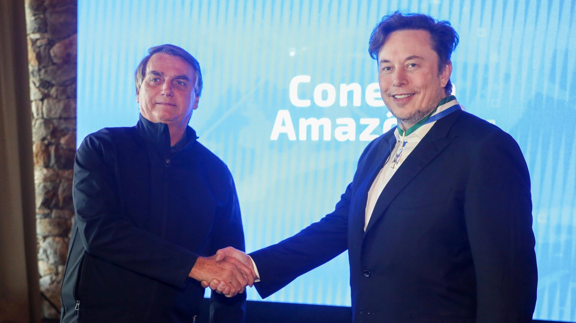 Elon Musk wird am 20. Mai 2022 in Porto Feliz, Brasilien, mit dem Verdienstorden der brasilianischen Verteidigung ausgezeichnet, als er dem damaligen brasilianischen Präsidenten Jair Bolsonaro die Hand schüttelt.