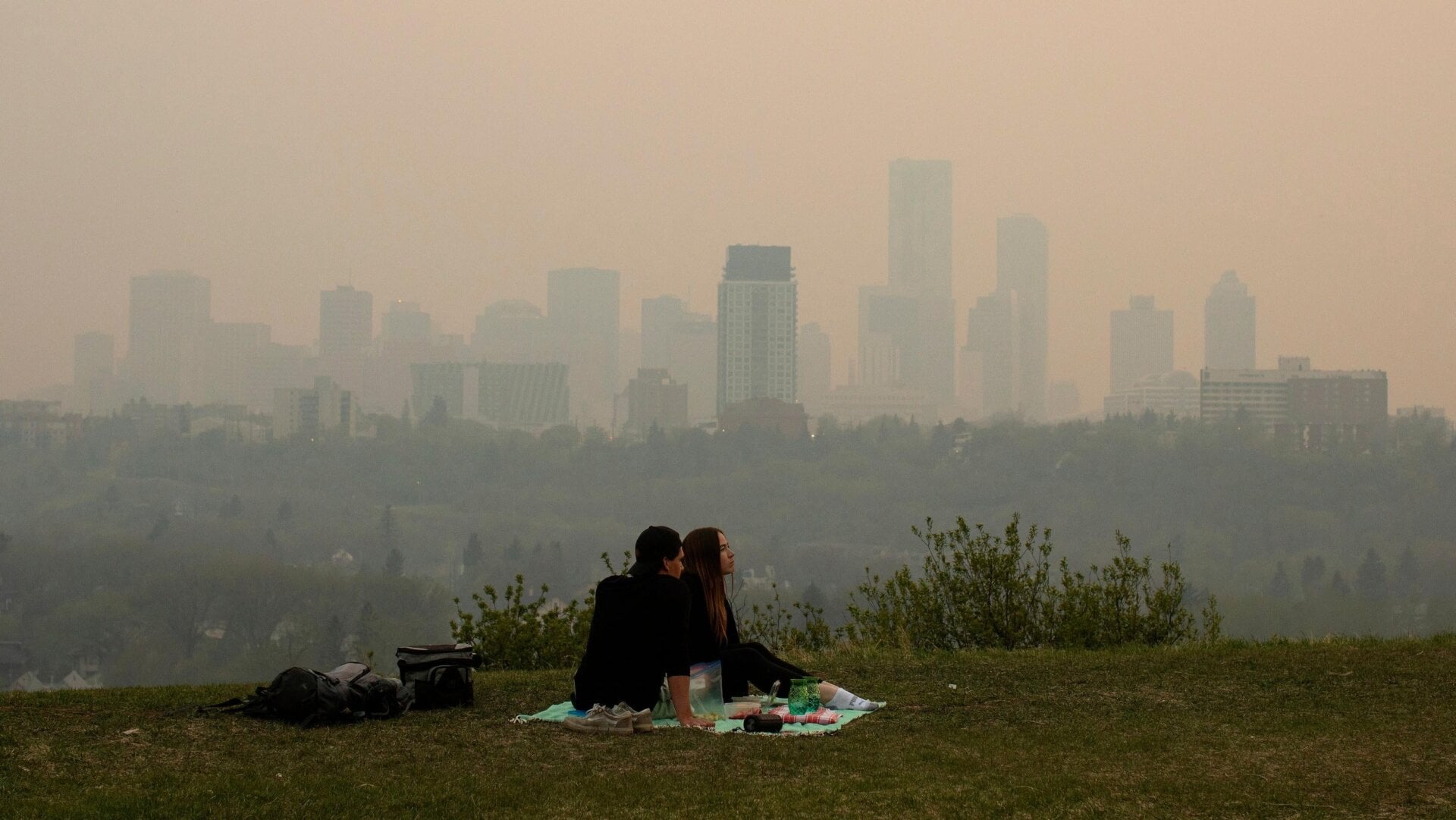 Rauch von Waldbränden bedeckt die Stadt, während ein Paar am 11. Mai 2024 in Edmonton, Alberta, ein Picknick macht.