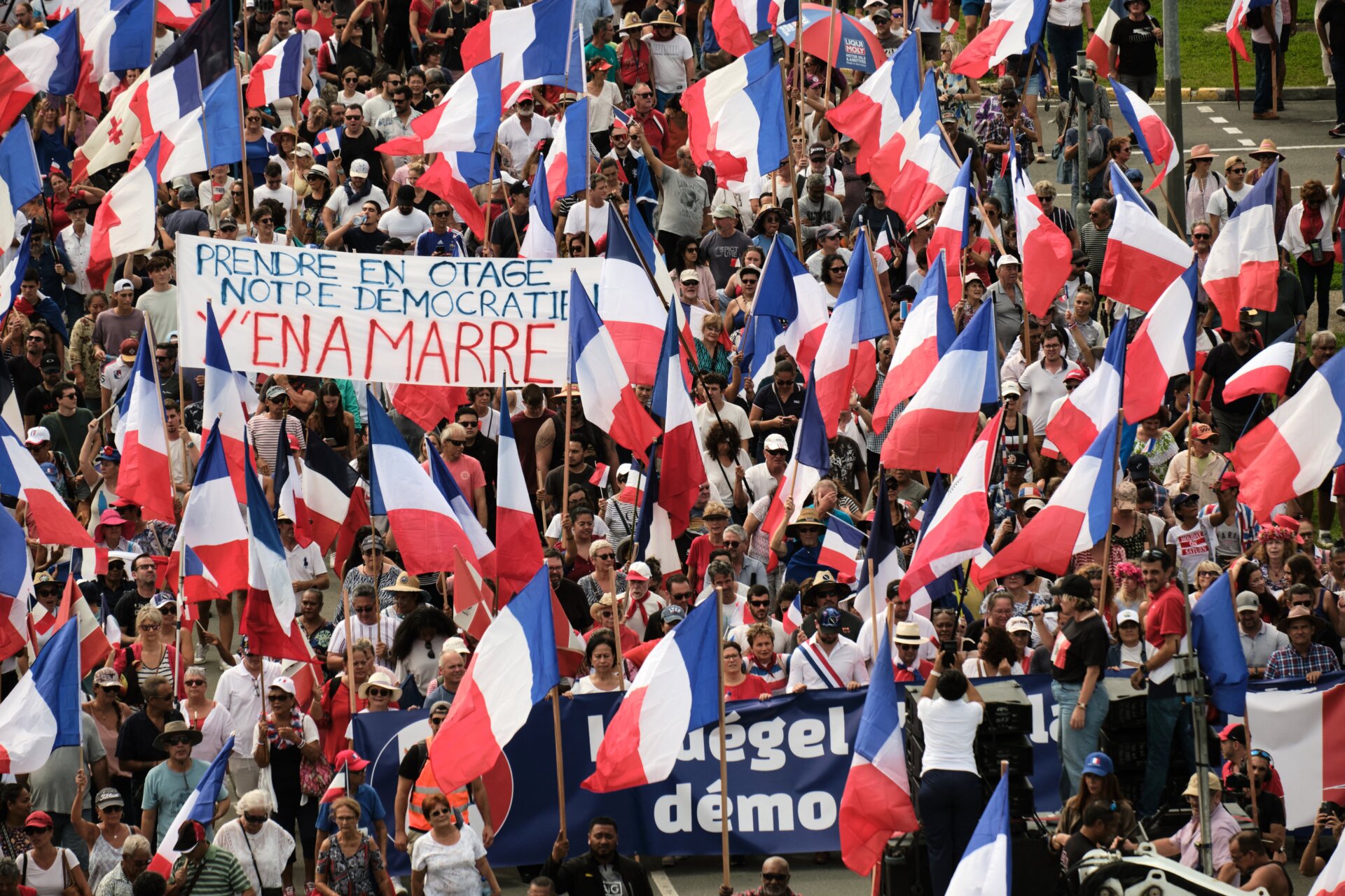 Demonstranten mehrerer loyalistischer Parteien schwenken französische Nationalflaggen und halten ein Transparent mit der Aufschrift „Prendre enotage notre democratien y’en a marre“ (Nehmt euch unsere Demokratie) hoch, während sie im Rahmen einer Demonstration zur Unterstützung der Erweiterung des Wahlkreises für die bevorstehenden Provinzwahlen in Neukaledonien, Noumea, am 13. April 2024 marschieren. 
