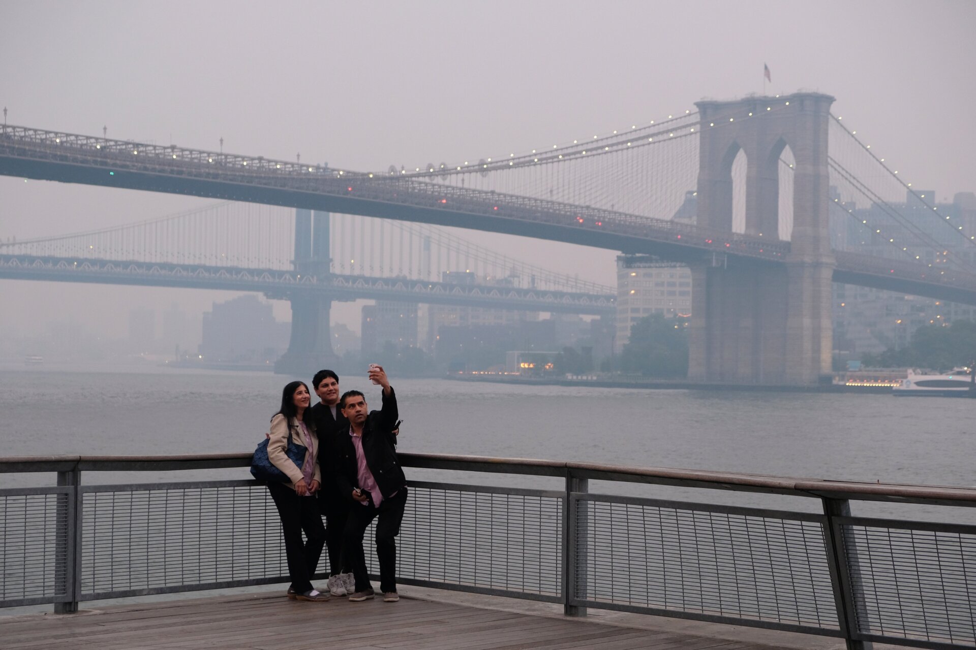 Eine Gruppe macht ein Selfie vor dem Hintergrund der Manhattan Bridge und  Brooklyn Bridge, rechts, in New York am Mittwoch, 7. Juni 2023