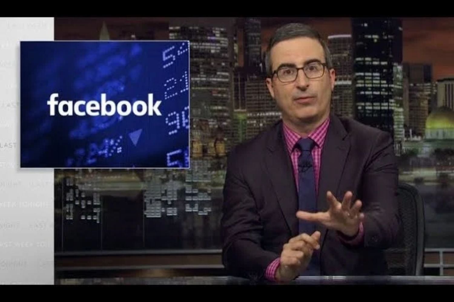 John Oliver an einem Schreibtisch mit einem Facebook-Logo zu seiner Linken.